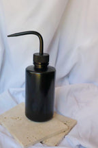 Black liquid dispenser bottle on a light-colored stone surface with a white fabric background