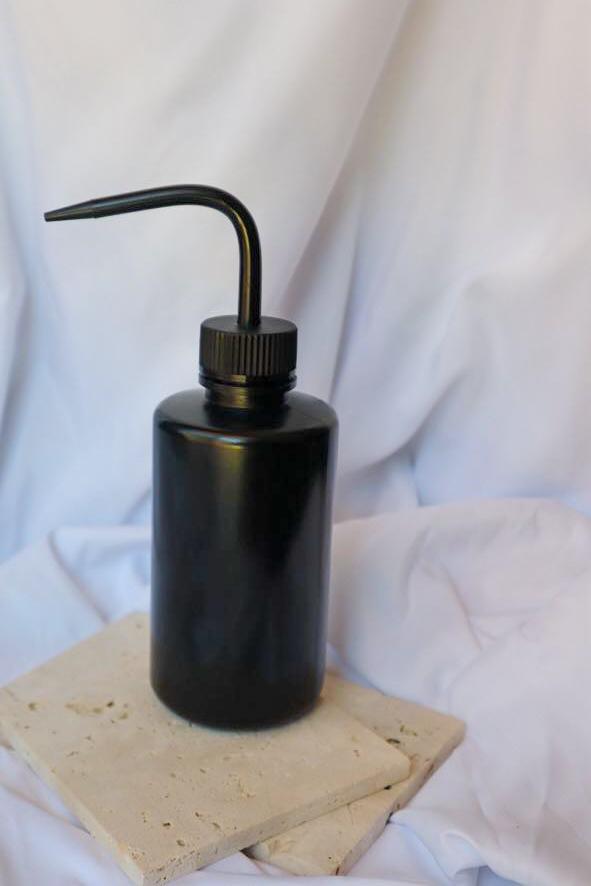 Black liquid dispenser bottle on a light-colored stone surface with a white fabric background