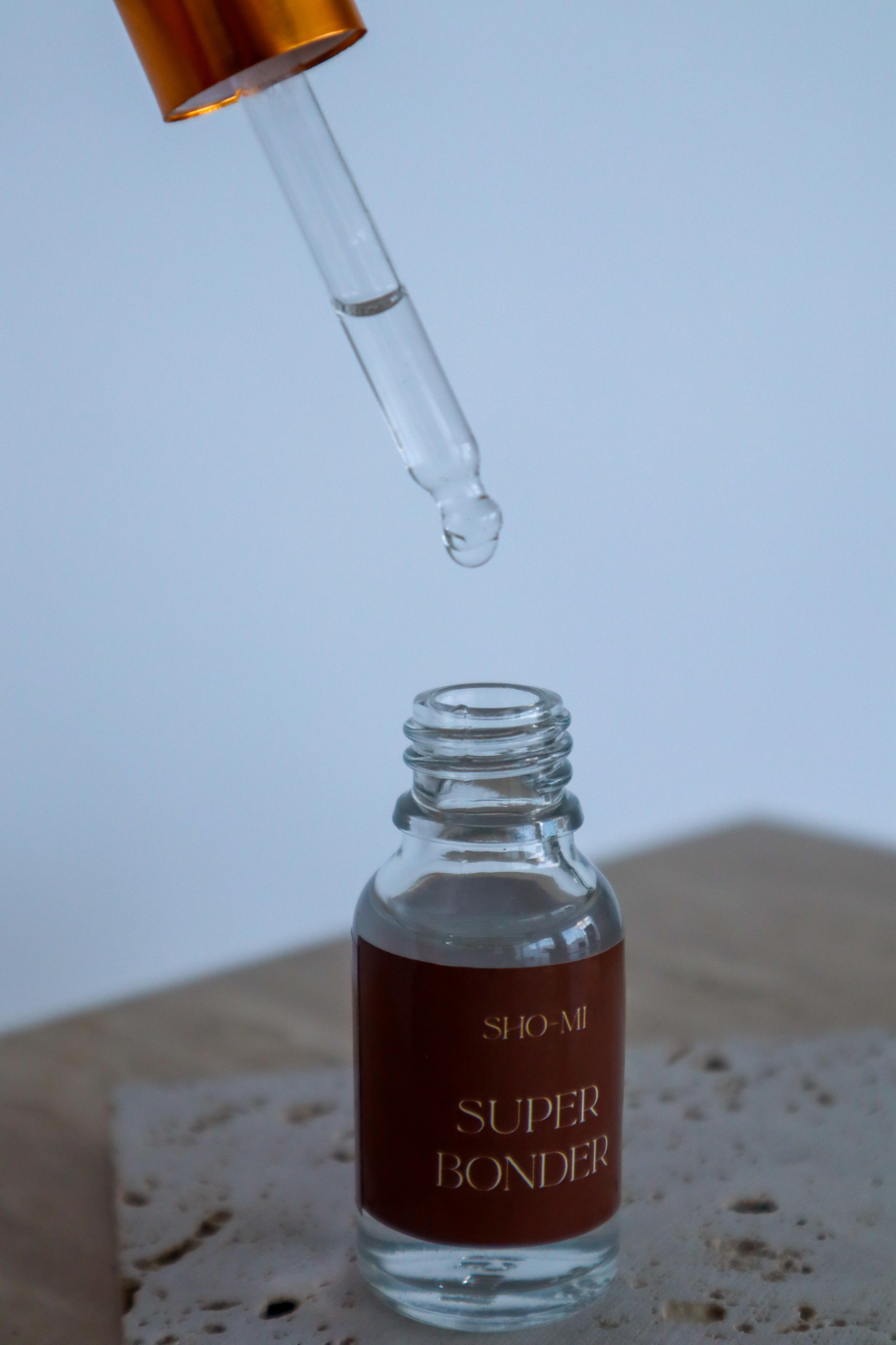 Glass dropper bottle labeled 'Super Bonder' with a droplet on a neutral background