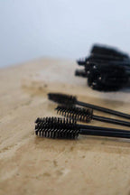 Black mascara brushes on a beige surface with a blurred background
