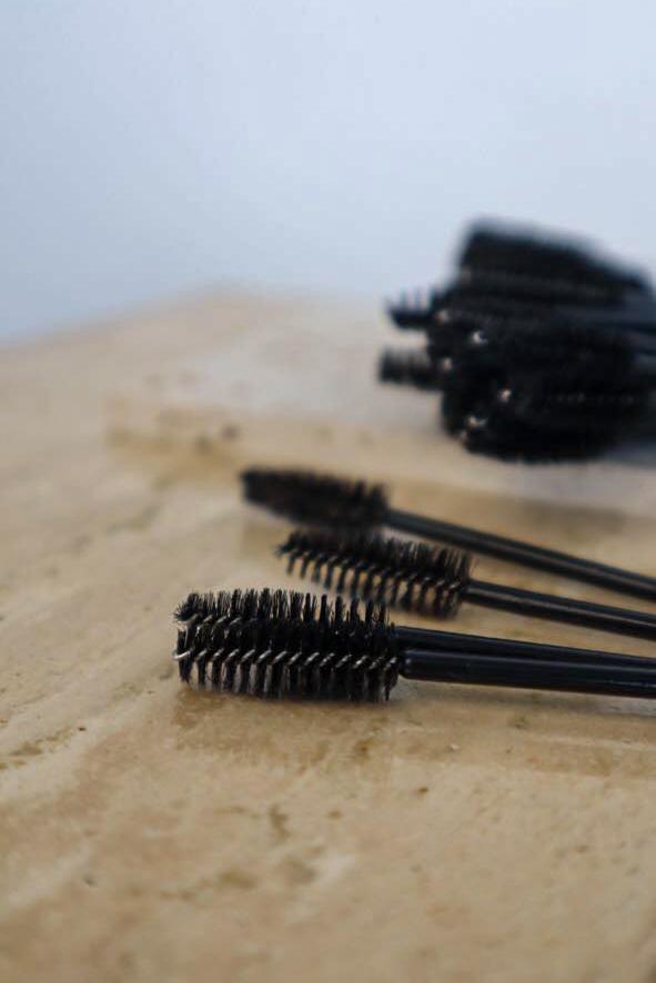 Black mascara brushes on a beige surface with a blurred background