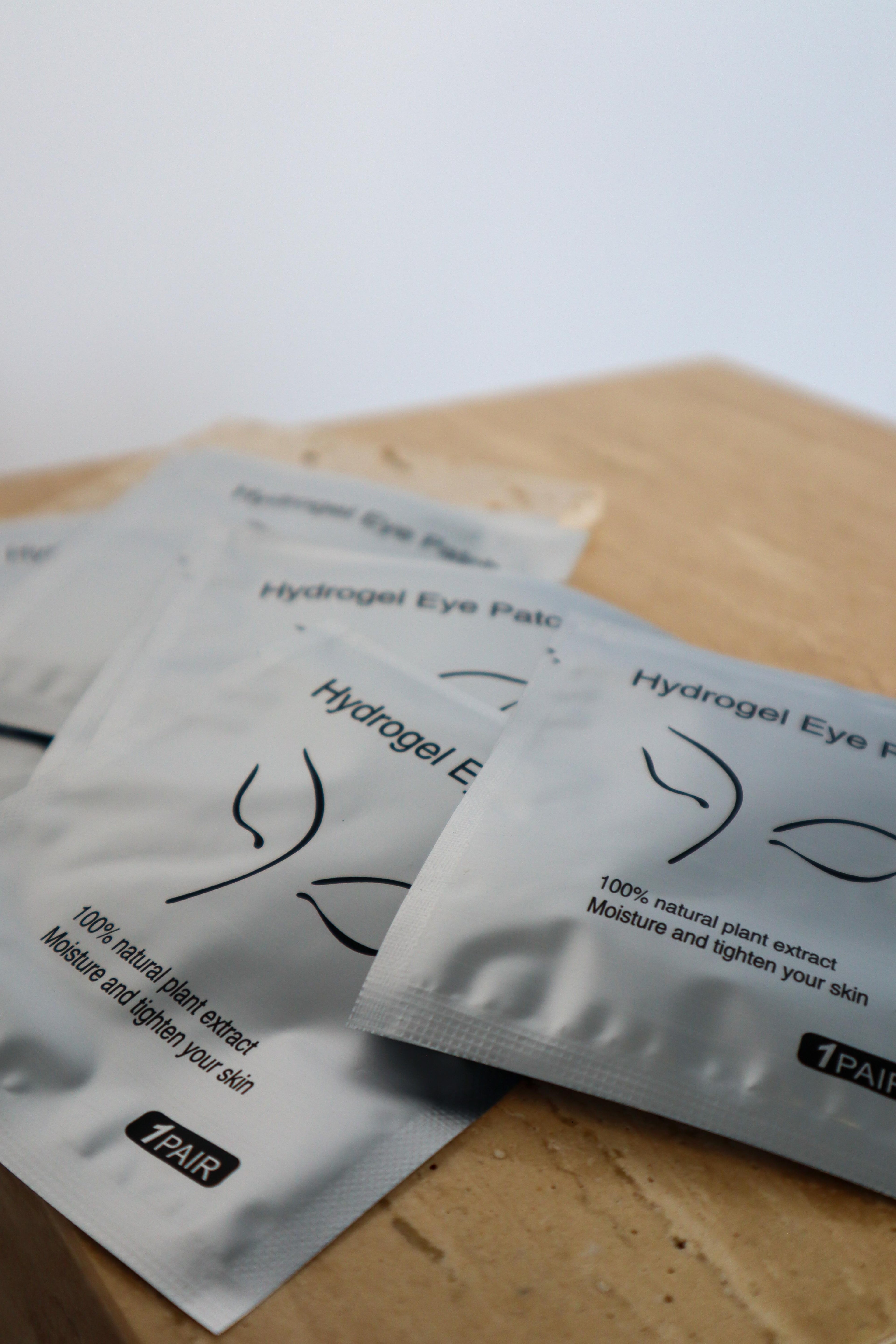 Multiple packages of hydrogel eye patches on a wooden surface with a blurred background.