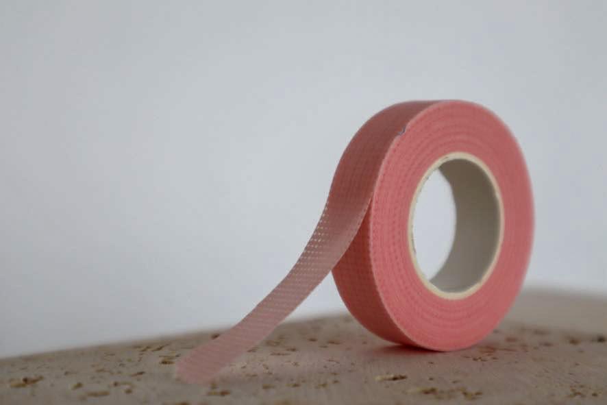 Roll of pink micropore lash tape on a textured surface with a light grey background
