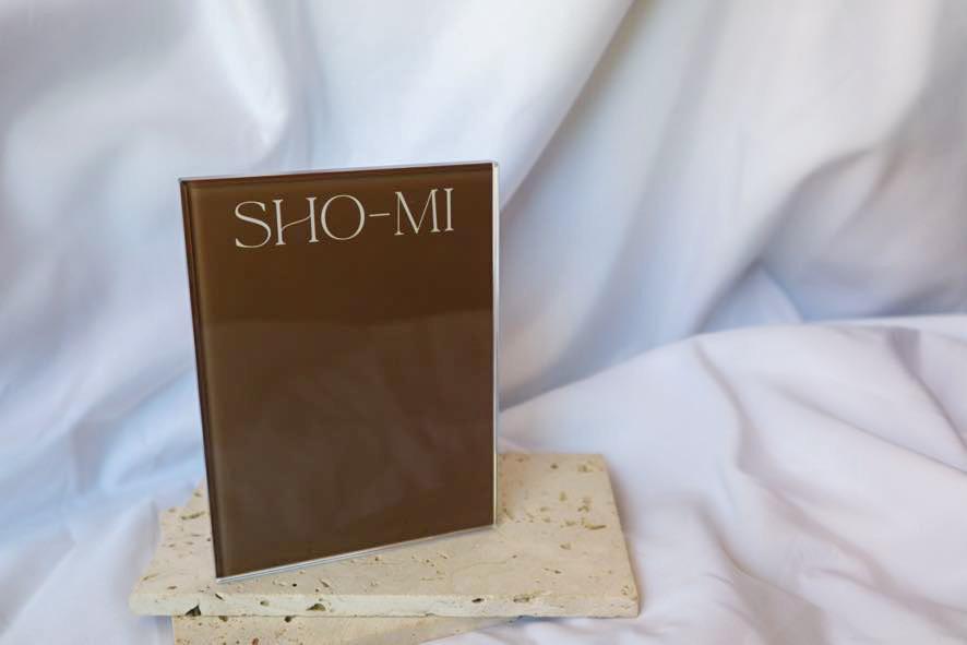 Crystal lash tile with SHO-MI text on a stone stand against a white fabric background