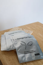 Hydrogel eye patch packets on a wooden surface with a white background