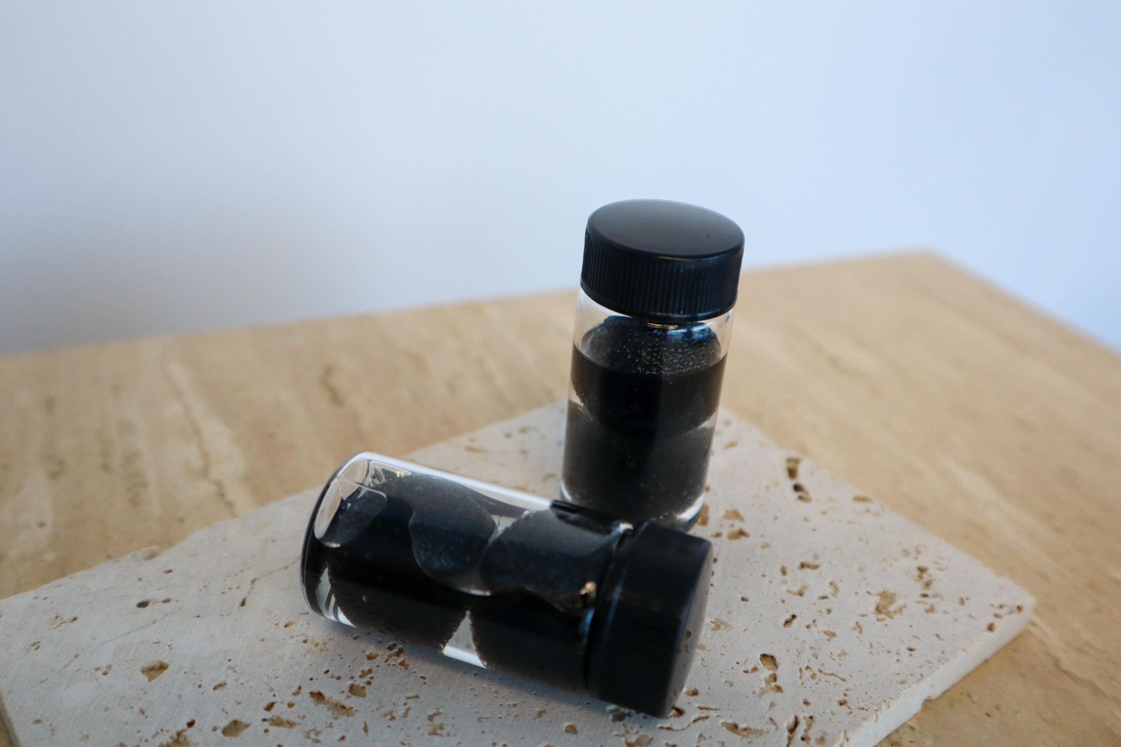 Two small clear bottles with black caps on a textured surface