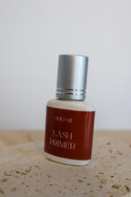 Bottle of Sho-Mi Lash Primer on a textured surface with a neutral background