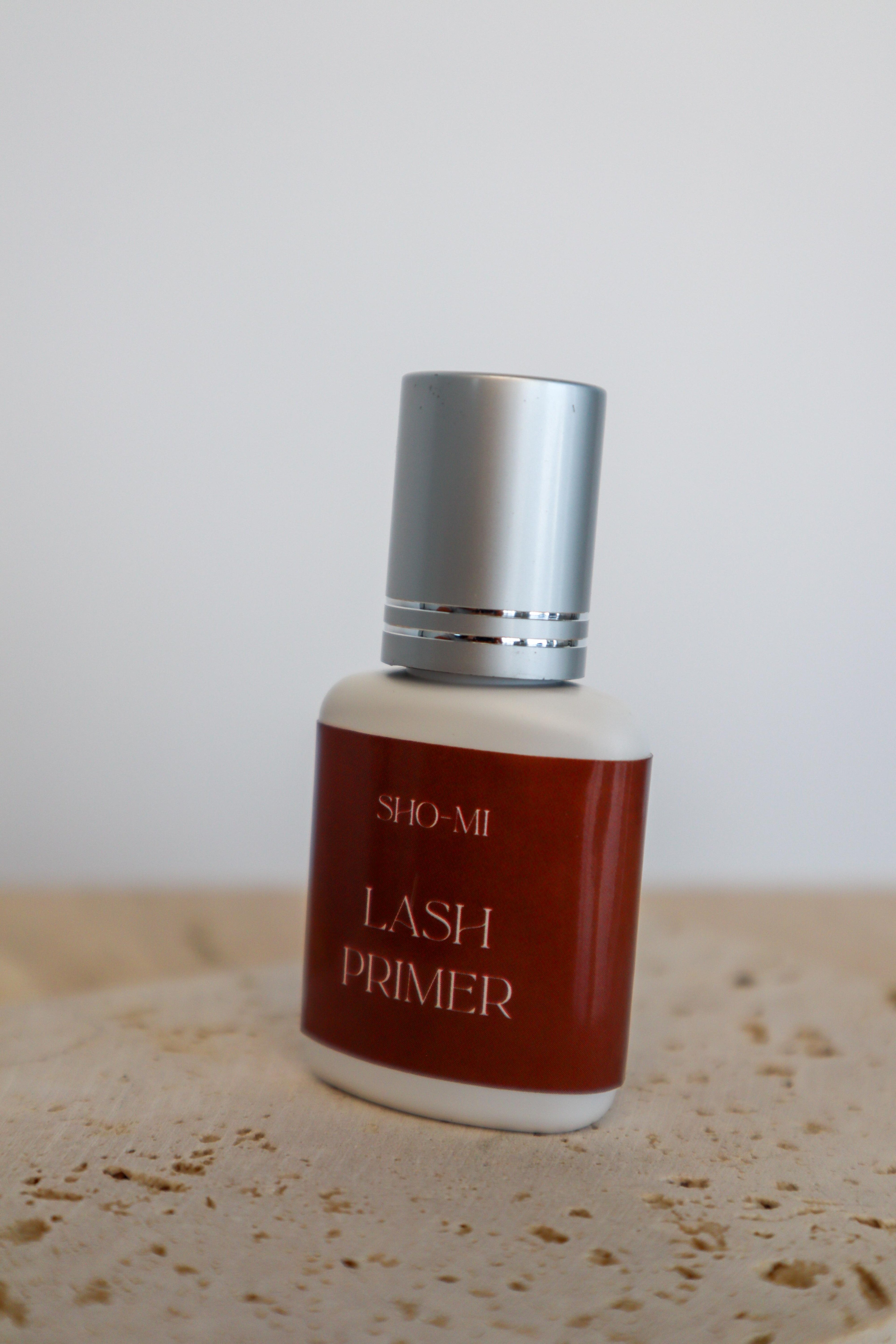 Bottle of Sho-Mi Lash Primer on a textured surface with a neutral background
