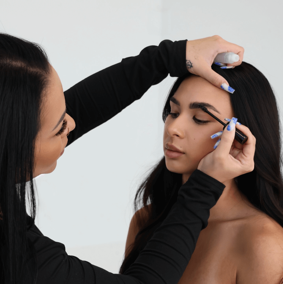 Makeup artist applying eyelash extensions to a model against a white background