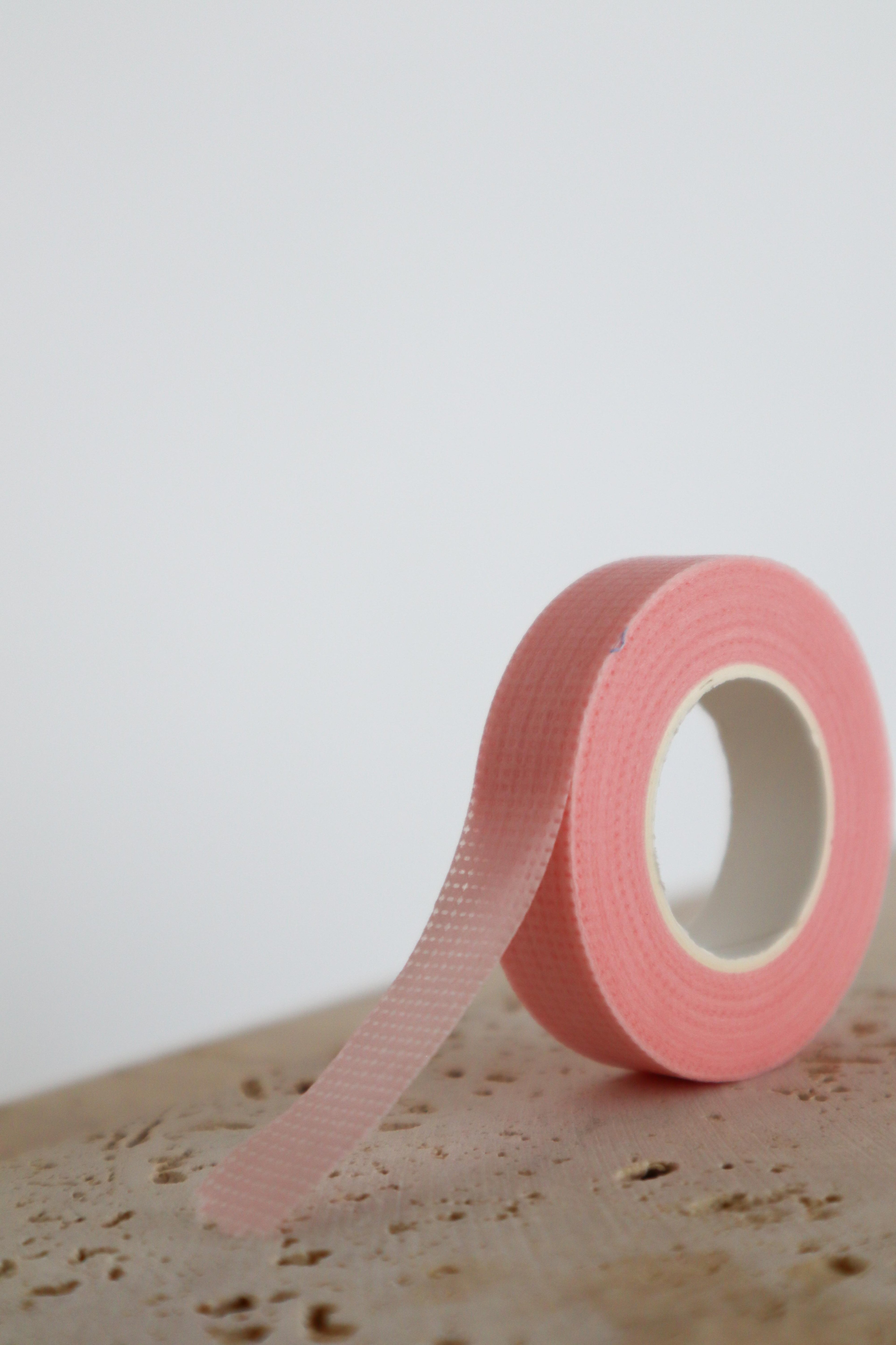 Pink micropore lash tape roll on a textured surface with a light grey background