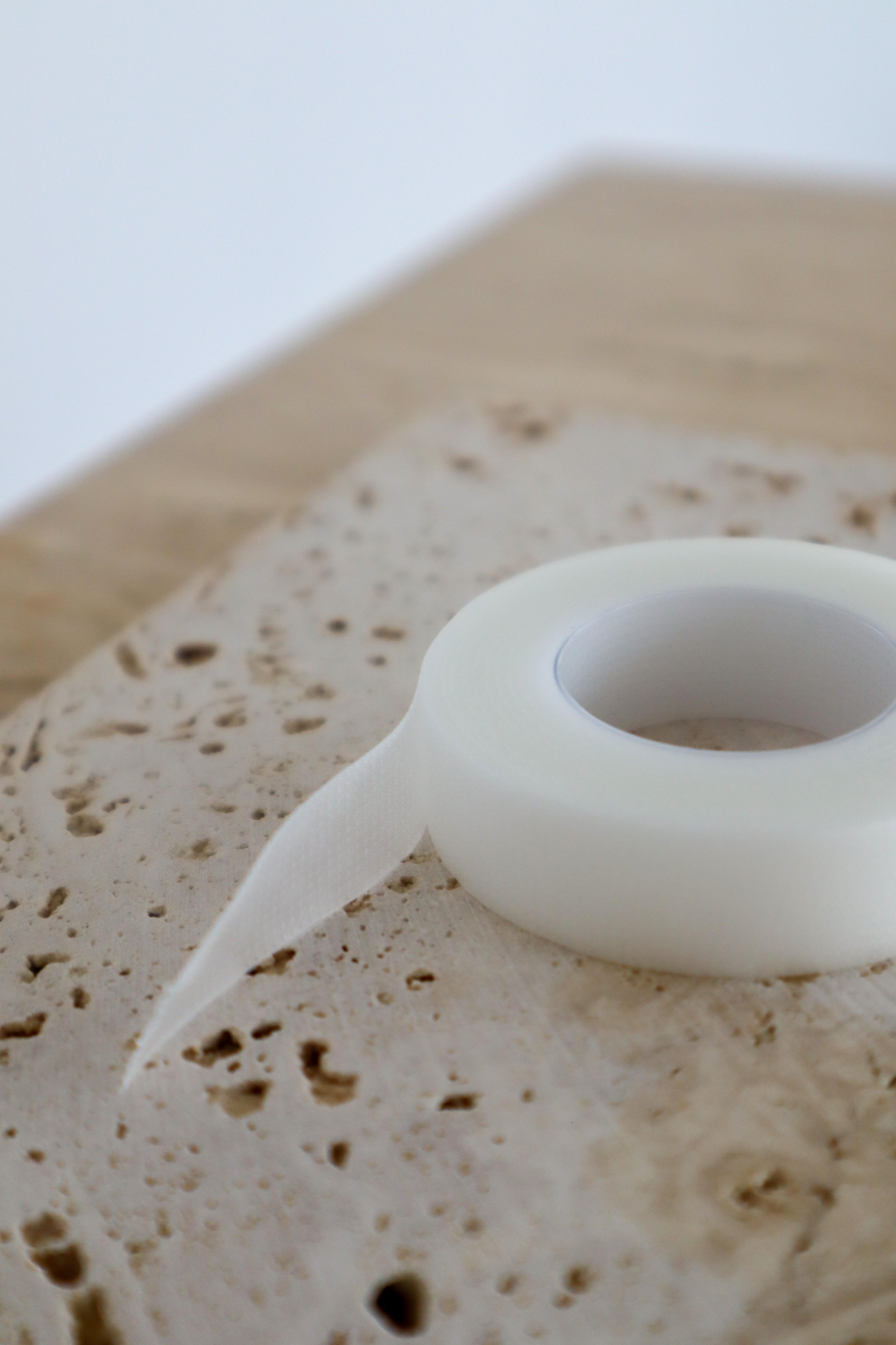 White micropore lash tape on a textured beige surface with a blurred white background