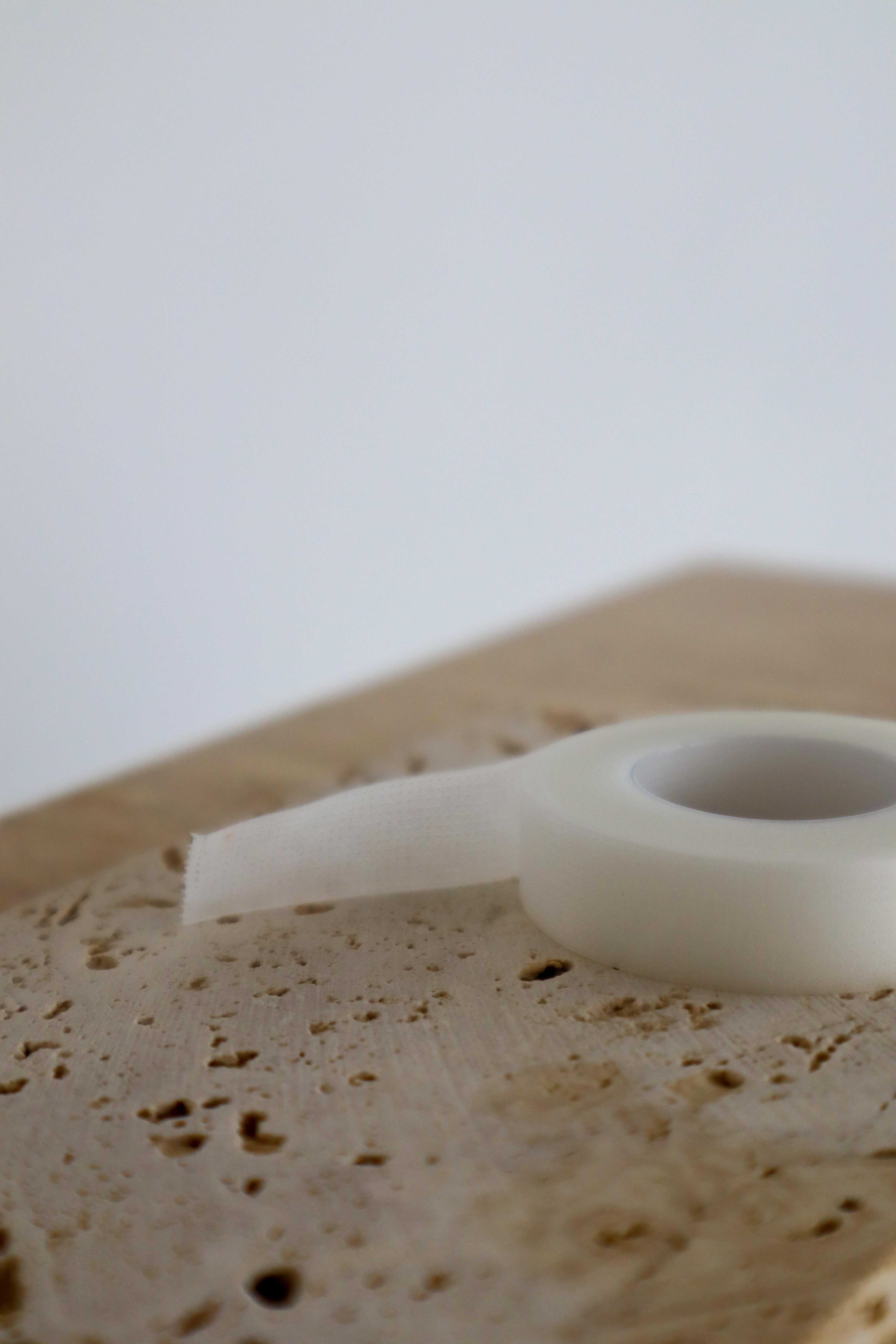 Close-up of a wooden surface with a roll of white micropore lash tape on a light background