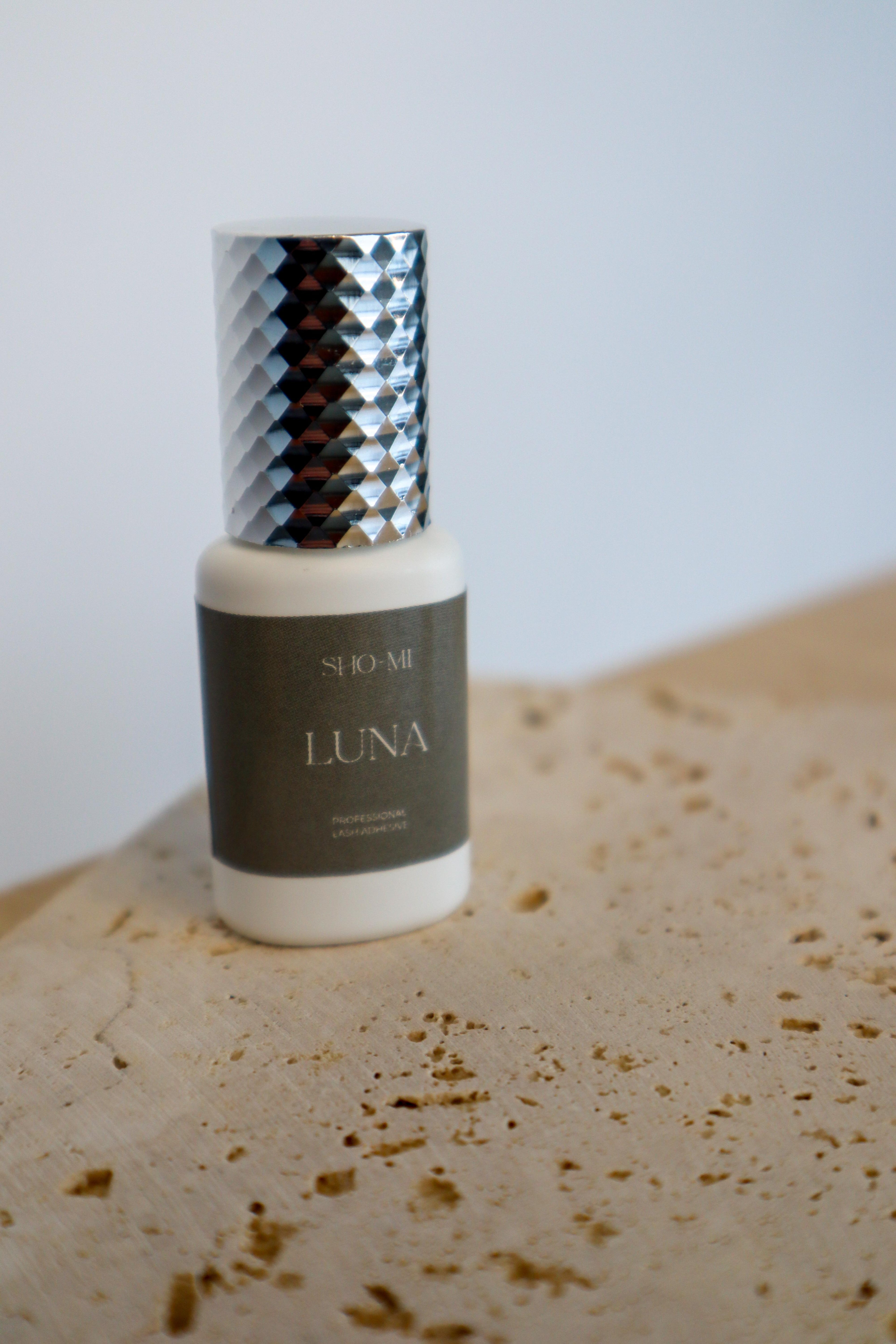 Lash extension glue bottle labeled 'LUNA' on a textured surface with a neutral background