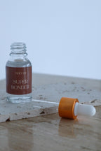 Clear glass bottle with dropper labeled 'Super Bonder' on a textured surface.