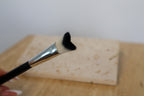 Lash cleansing brush with black bristle tip held over a wooden surface