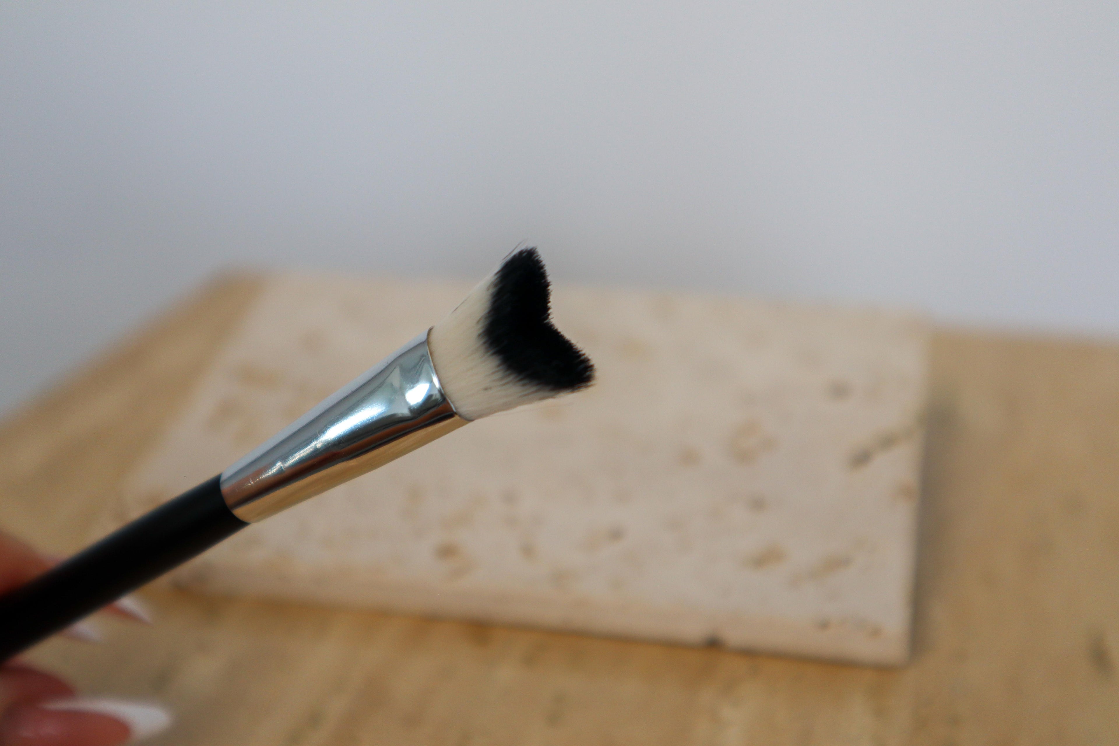Lash cleansing brush with black bristle tip held over a wooden surface