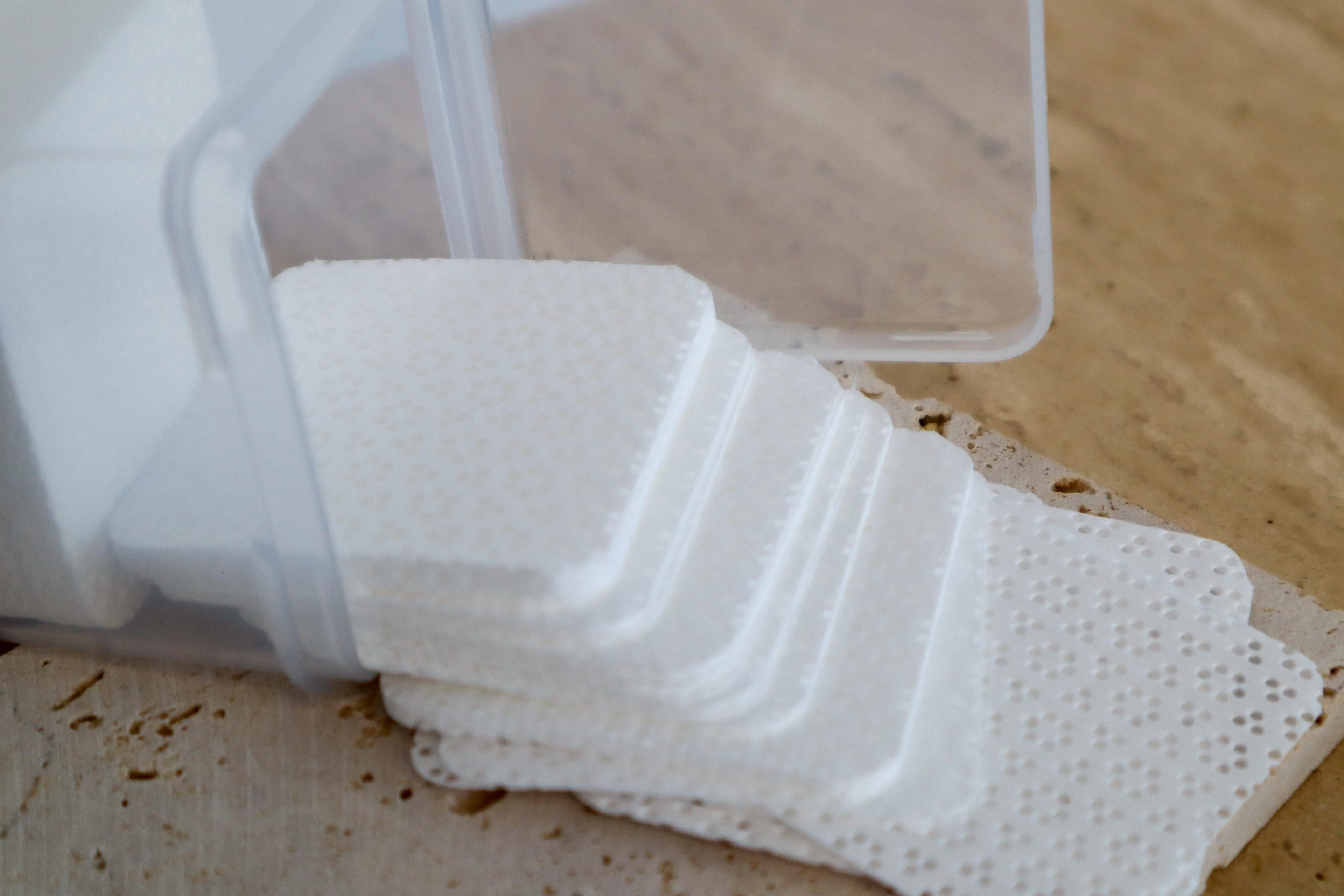 White lint free wipes on a wooden surface within a clear container.
