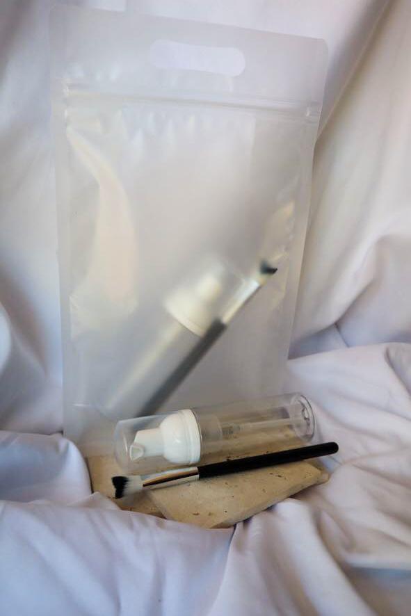 Cosmetic bag with a bottle, brush, and small container on a white surface