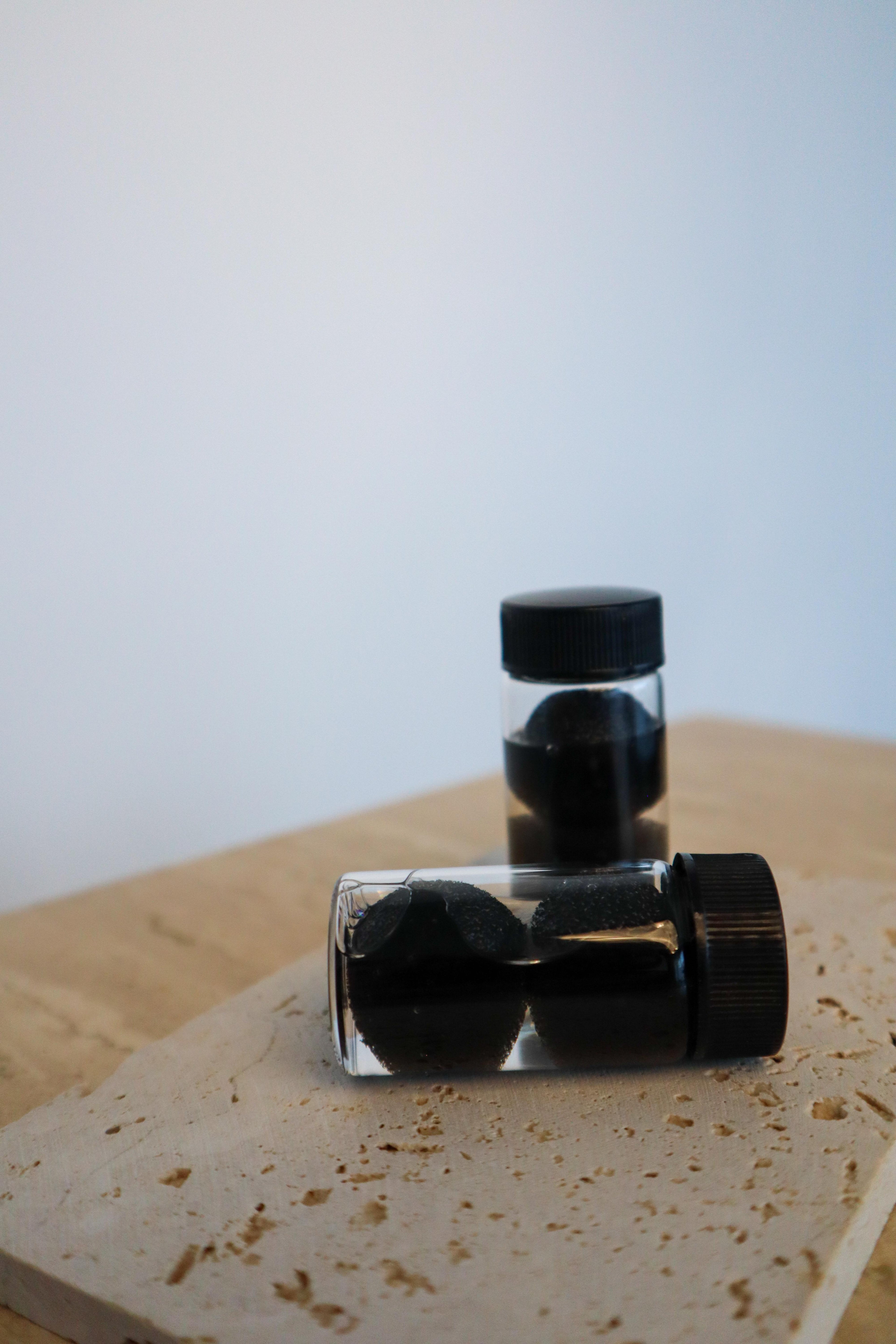 Two small clear bottles with black contents on a textured surface
