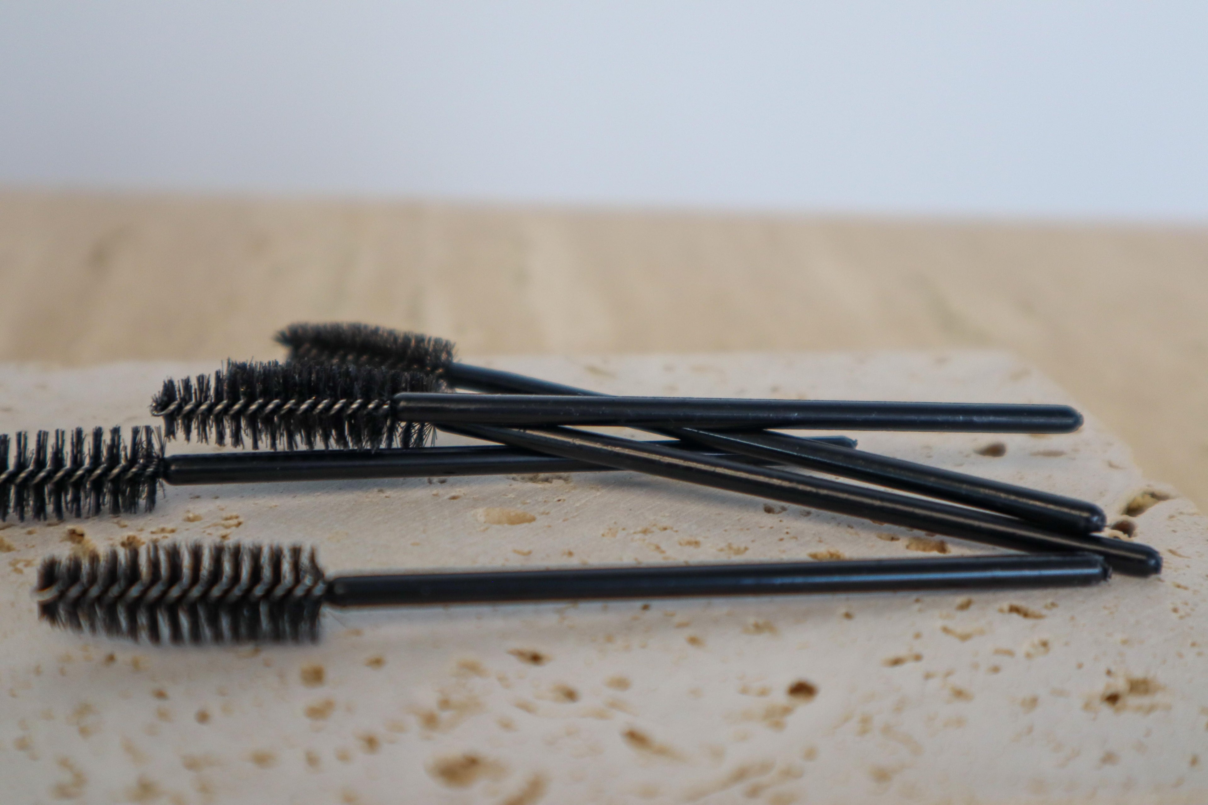 Black mascara brushes on a textured surface with a blurred background