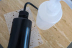 Black and white lash cleansing bottles on a wooden surface