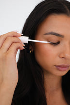 A woman with dark hair is applying SHO-MI lash growth serum