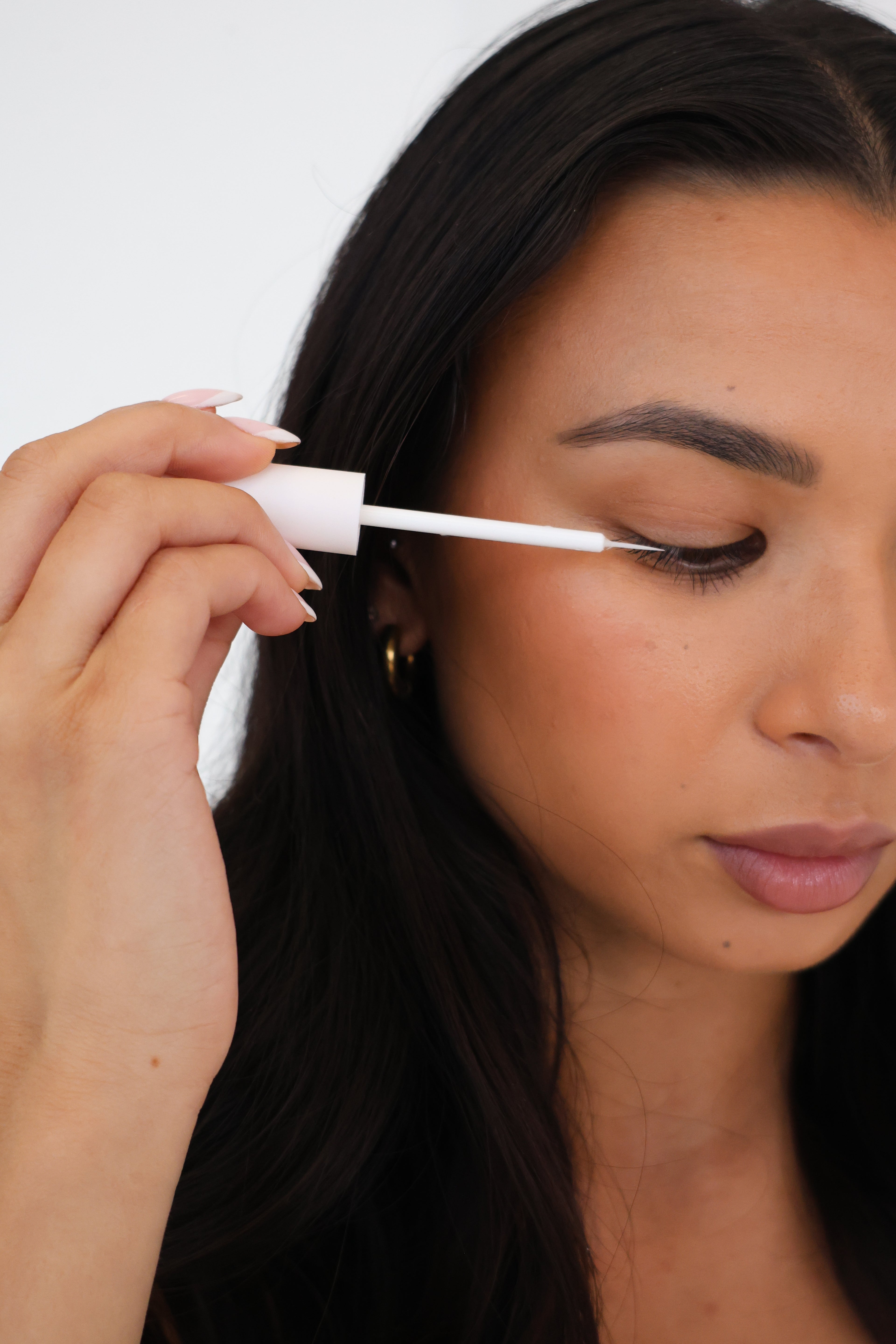 A woman with dark hair is applying SHO-MI lash growth serum